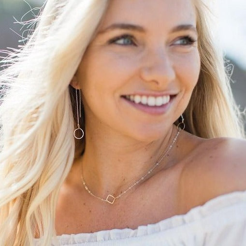dainty handmade necklace with tiny gold square on silver chain, on pretty blond model with beautiful smile wearing white off the shoulder top and matching circle threader style earrings